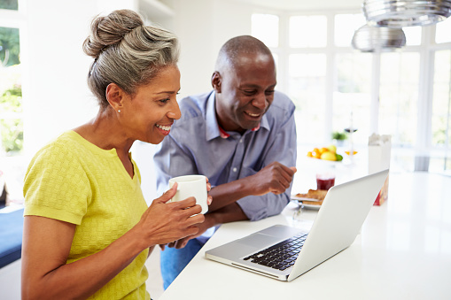 A black middle aged couple utilizing insurance services on a laptop in the kitchen.