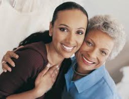 Two women hugging each other in front of a white dresser at Aware Insurance Services.
